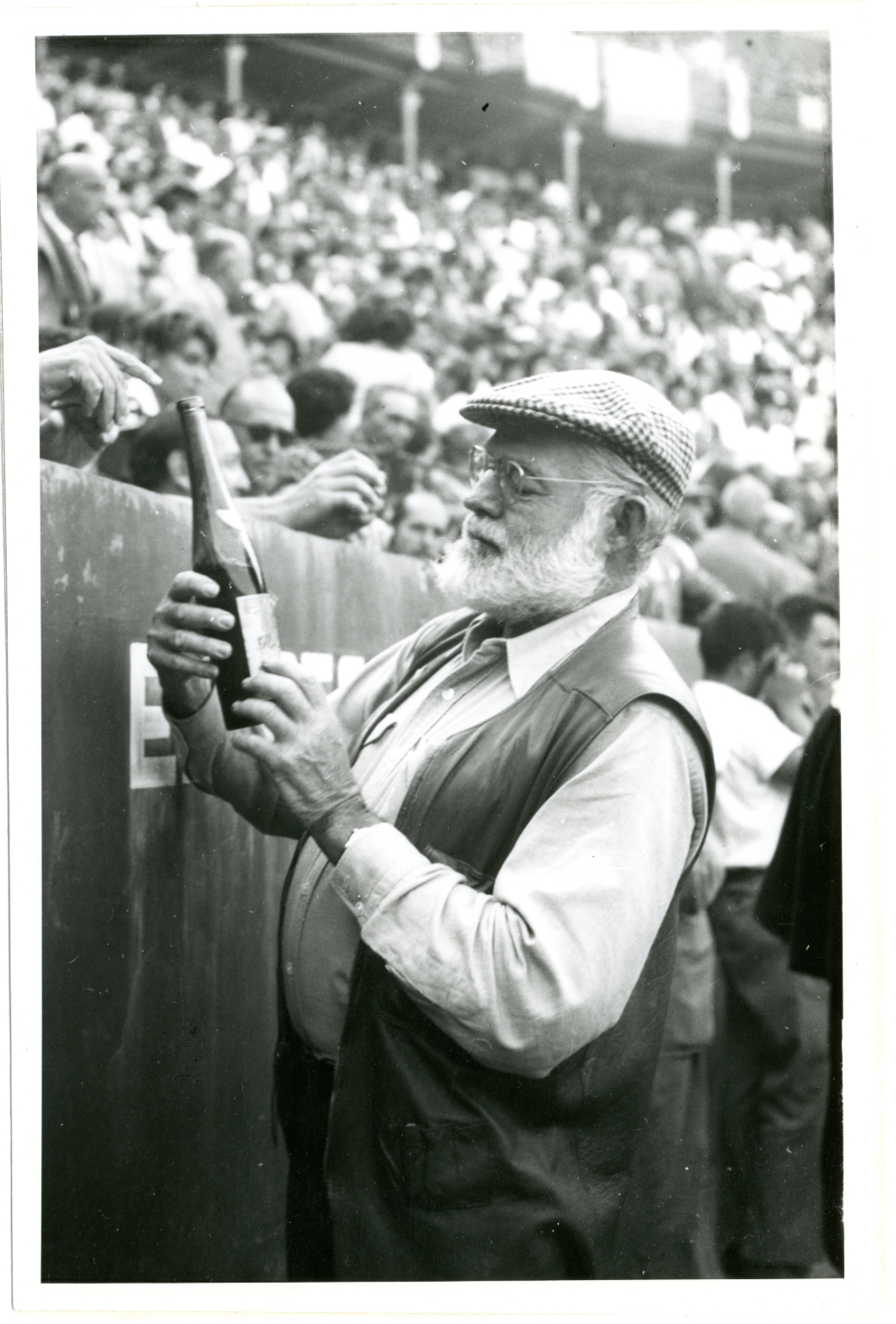 Hemingway at Bullfight Inspecting Wine Bottle